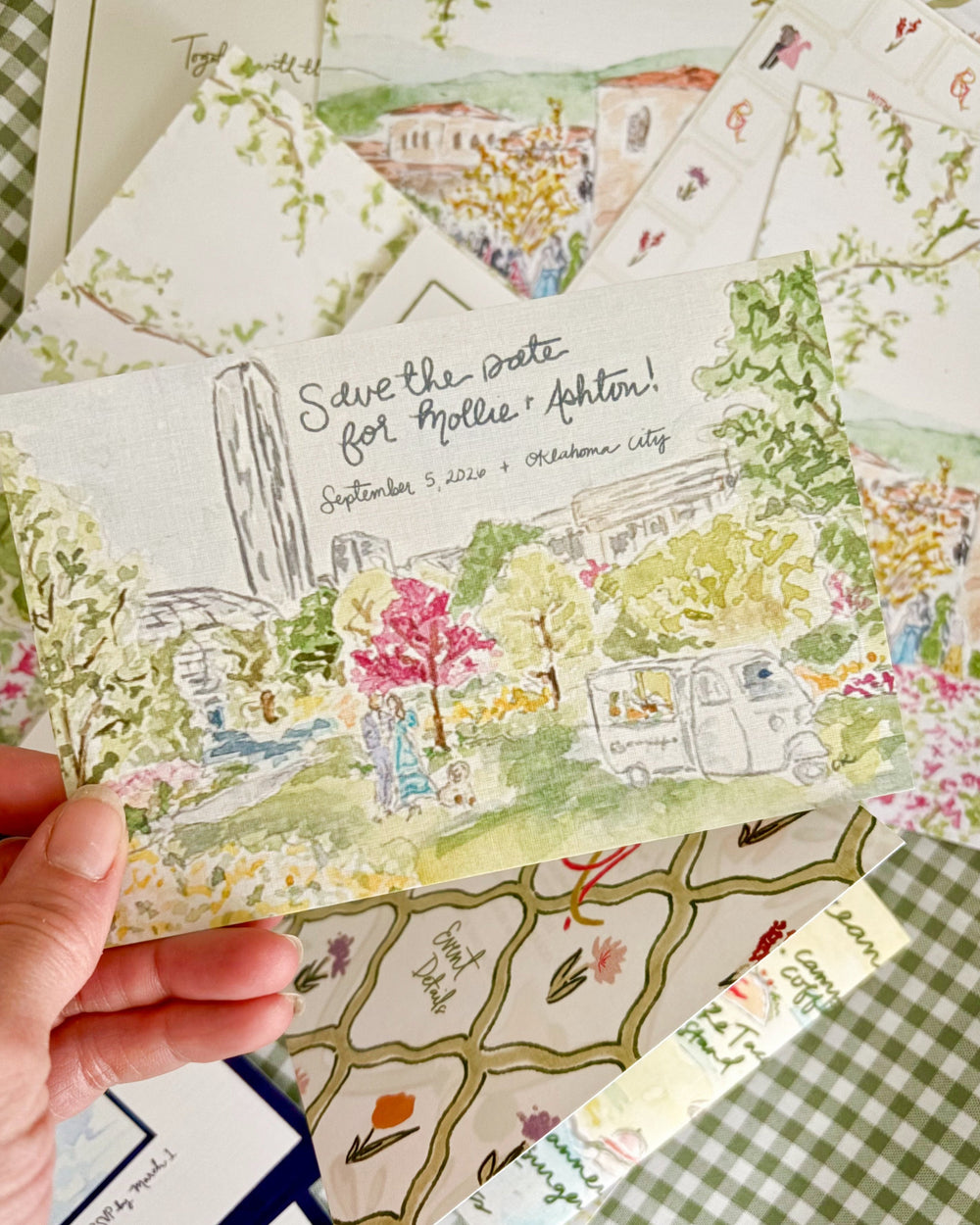 Hand holding a wedding invitation with scenic design and text.